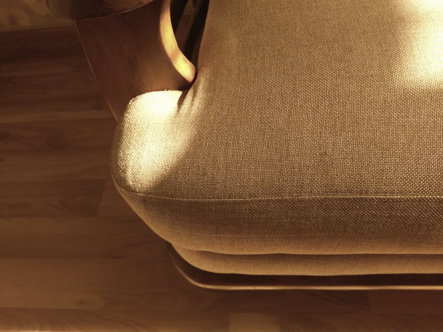 A person holding a yellow portable surface cleaning or sanitisation device, with black vent slats on the front, positioned over a textured, patterned carpet or rug with shades of beige, green, and ora